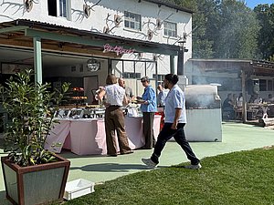 Im Hintergrund wird bei Sonnenschein gegrillt und eine Person geht im Vordergrund durchs Bild.