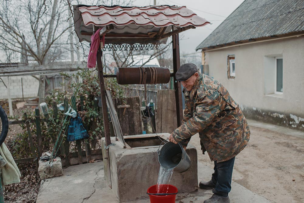 [Translate to English:] Mann schöpft Wasser aus Brunnen